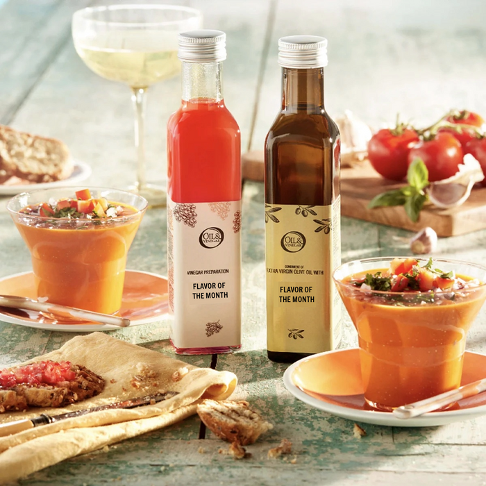 Two bottles, one containing oil and the other vinegar, presented on a table with food around them, indicating a culinary subscription service.