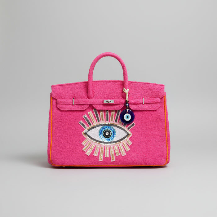 Bright pink terry beach bag with eye design and charm held by hand in outdoor greenery