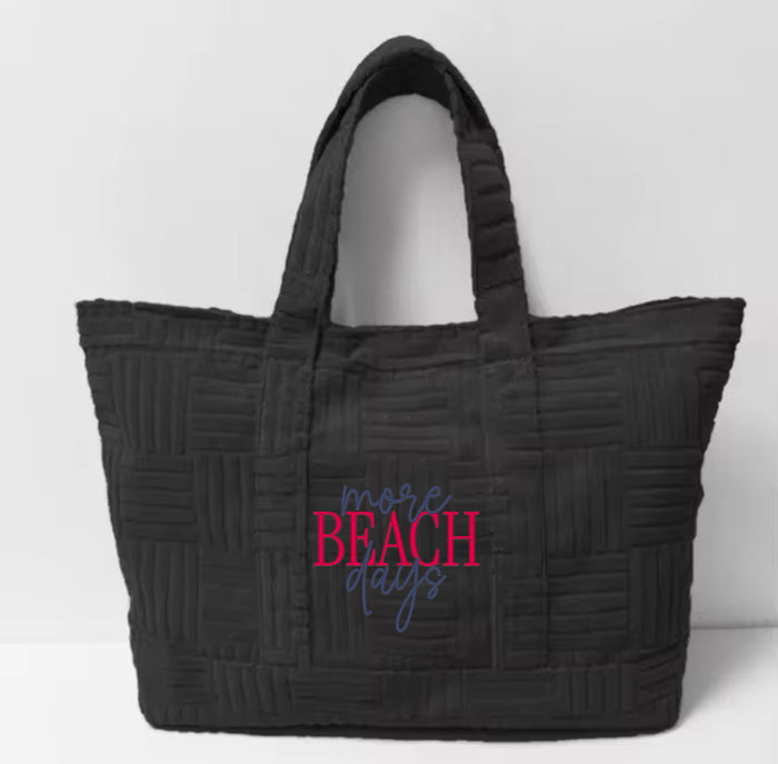 Black terry cloth beach tote bag with quilted texture and 'more beach days' text design