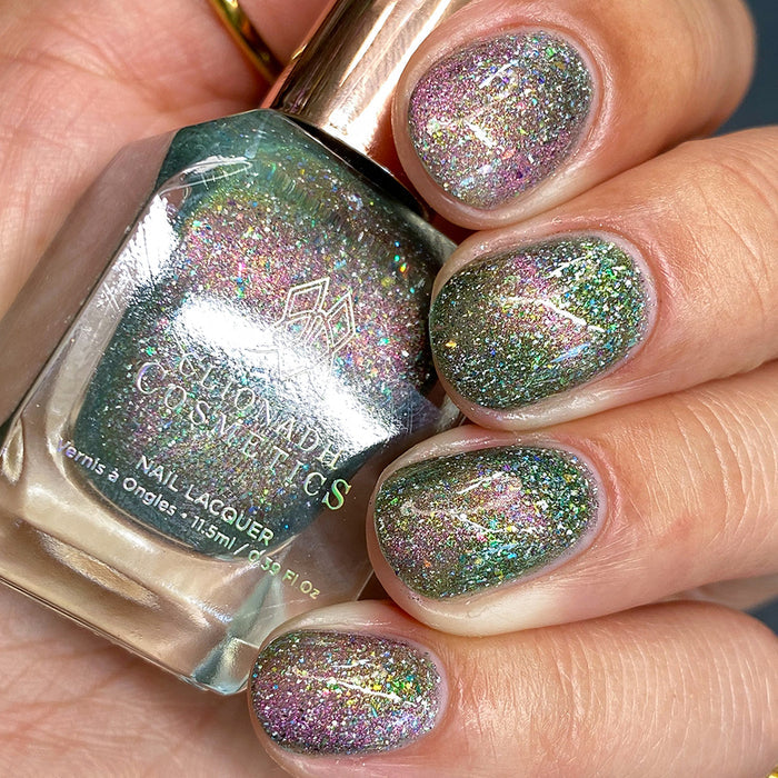 Close-up of nails painted with Th1rt3en Nail Lacquer on fair skin tone. Hand is holding polish bottle.