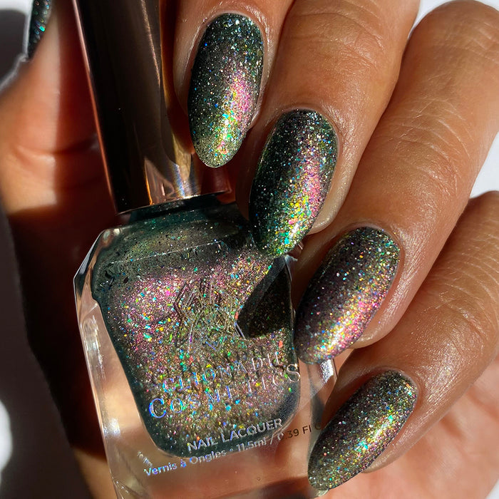 Close-up of nails painted with Th1rt3en Nail Lacquer on medium skin tone. Hand is holding polish bottle.