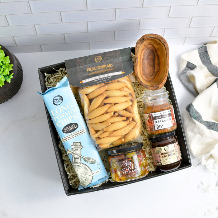 Gift box  filled with chips, dip mixes, a spread, and other snacks on a white surface.