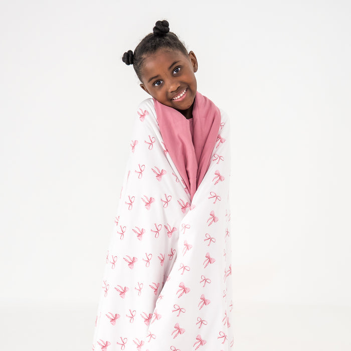 Child wrapped in a white blanket with pink patterns on a white background