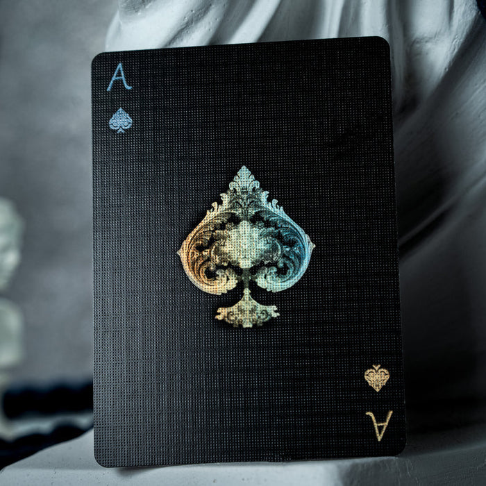 Black card with a gold and blue spade symbol held by a person against a blurred background