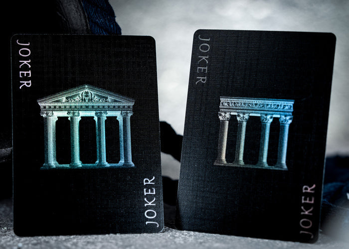 Two black playing cards with 'Joker' text and architectural design on a dark background
