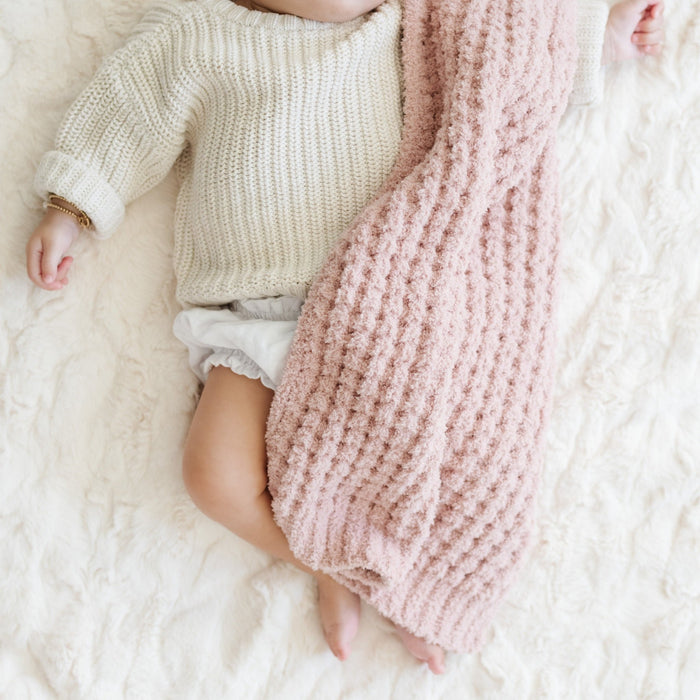 Baby girl sleeping in crib with link waffle knit blanket.