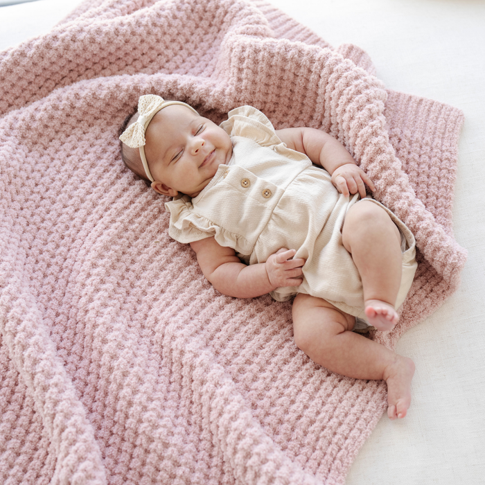 Baby girl sleeping on a pink waffle knit receiving baby blanket.