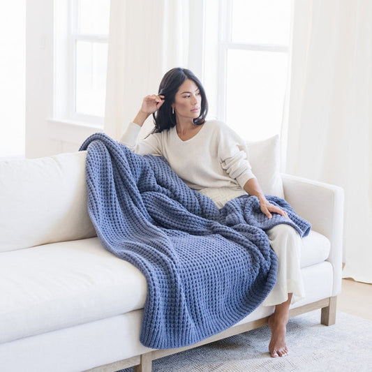 Person cozily wrapped in a blue waffle knit throw blanket, sitting on a couch.