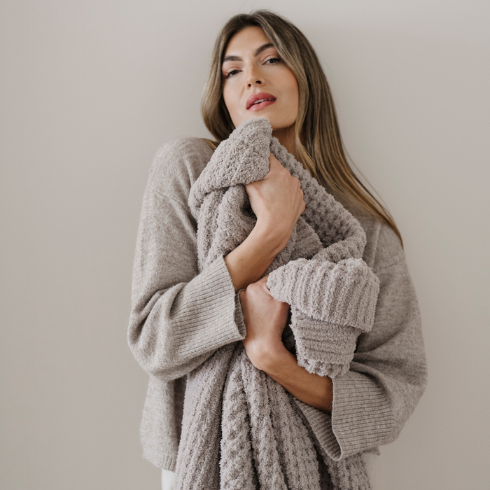 A woman holds a light tan waffle knit Saranoni blanket that is a throw blanket. This soft blanket is very luxurious and used for gifting, relaxing, or home decor.