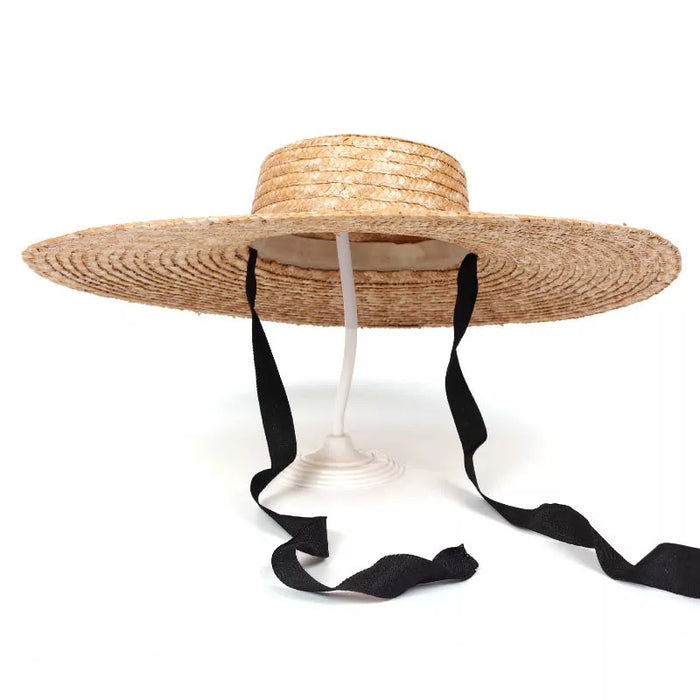 Wheat straw hat with ribbon in black featuring wide brim and adjustable ties on display stand
