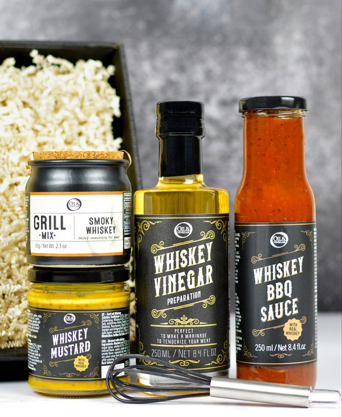 Set of whiskey-themed condiments with a black box filled with crinkle paper on a gray background