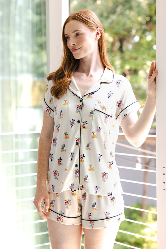 Model posing Women's Short Sleeve Pajama Set in Mickey Mouse & Friends print standing in front of glass door