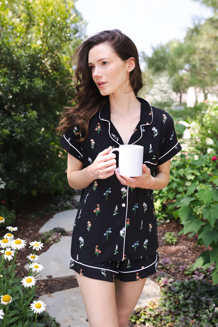 Woman wearing a short sleeve black pajama set with wildflower pattern holding a coffee cup