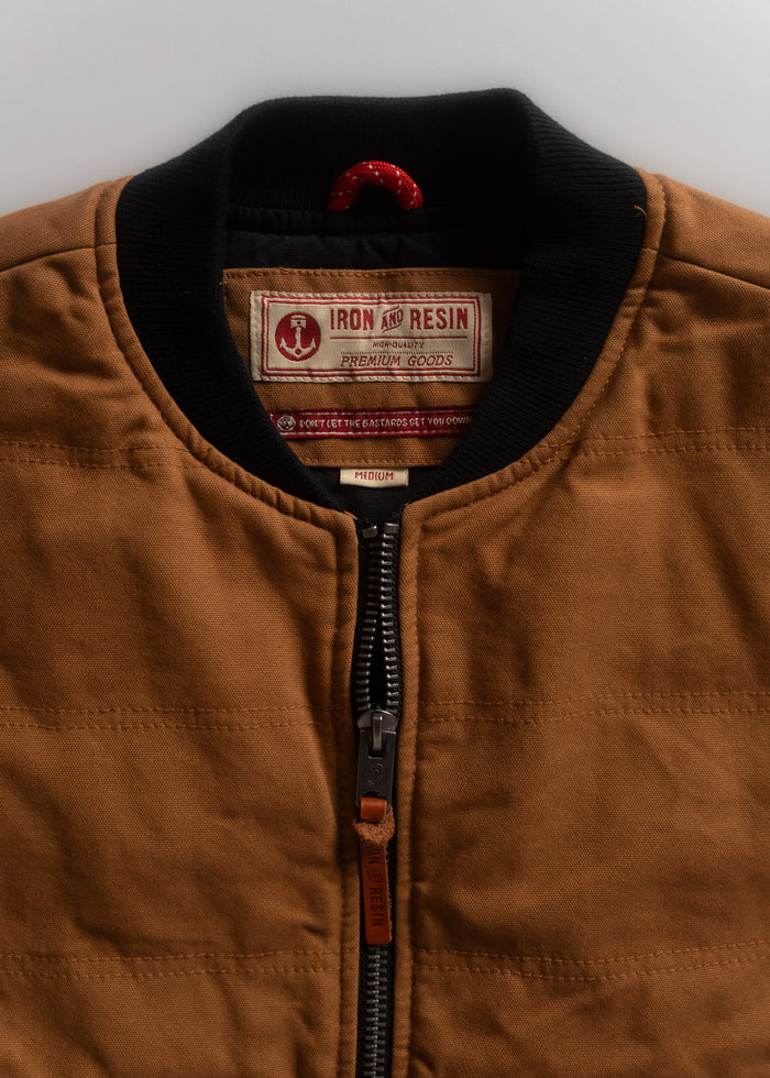 Brown jacket with black collar, featuring Iron and Resin label. Visible zipper and red hanging loop. Size medium.