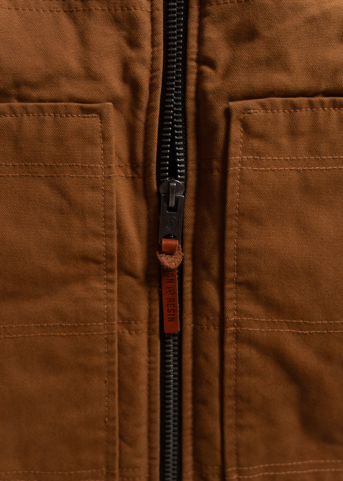 Close-up of a brown fabric jacket with a black zipper and a leather pull tab labeled "Iron and Resin," highlighting its texture.