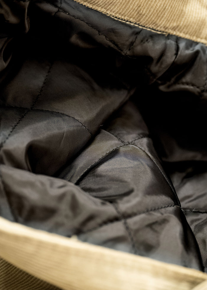 Close-up of a quilted black lining inside a beige corduroy jacket, showcasing texture and stitching details.