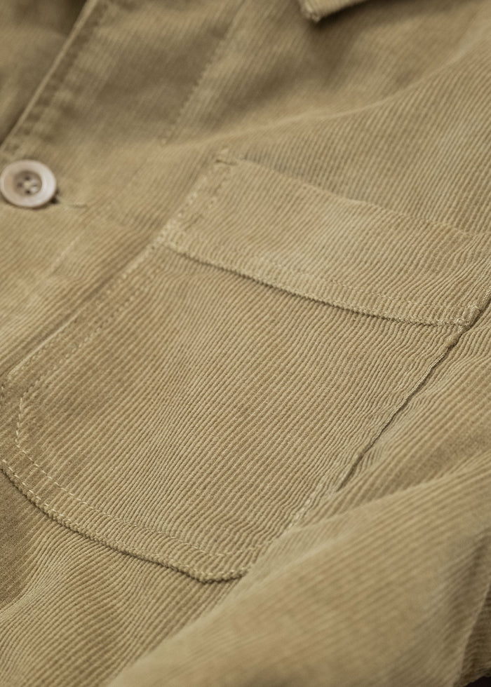 Close-up of a beige corduroy shirt pocket with a button, highlighting the texture and stitching details of the fabric.