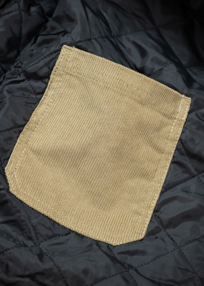 Tan corduroy pocket sewn onto black quilted fabric, showcasing texture contrast and stitching detail.