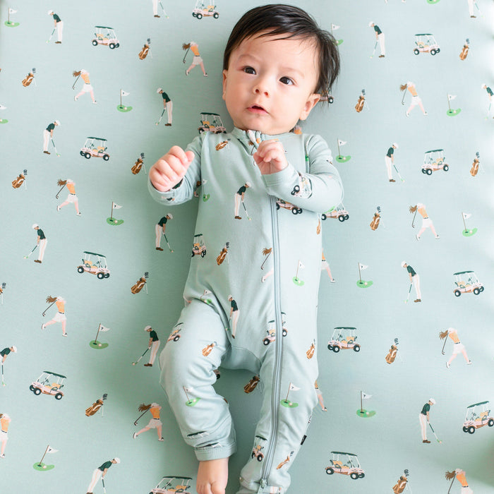 Infant wearing Zippered Romper pajamas  laying on Golf Crib Sheet