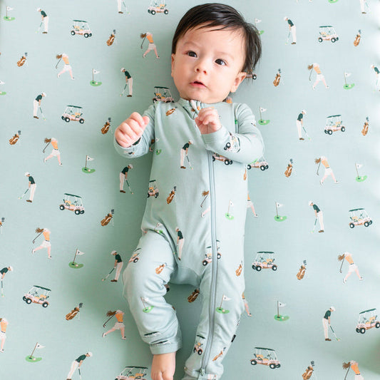 Infant wearing Zippered Romper pajamas  laying on Golf Crib Sheet