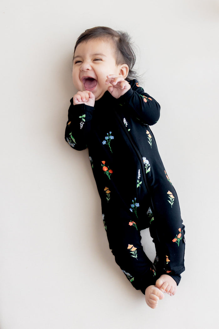 Baby smiling in Zippered Romper in Midnight Wildflower print lying on an oat crib sheet